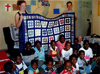 Former Lopez high school students Rebecca De Graaf (l) and Todd Foley (r) presenting a Lopez-made quilt to Malawi children in 2003.
