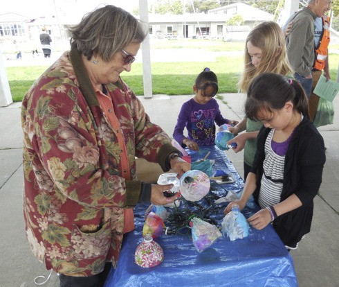 Volunteer artist Debbie Collins helps students turn plastic bottles and tissue paper into festive party lights