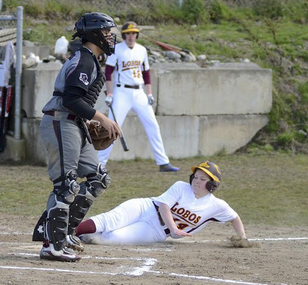 Lopez’ Mikayla Johnson (14) slides in safely at home against Lummi in the Lobos’ 8-6 loss on April 1.  Exchange student Jurgen Sande (13) watches from the on deck circle.