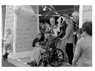 Market co-owner Aaron Dye (center) kneels next to co-owner Bill Carpenter’s chair as he cuts the ribbon in the opening ceremony for the new Lopez Village Market.