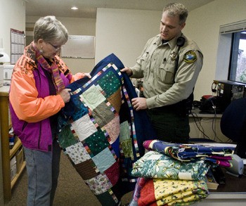 Carole Knutsen hands Deputy Scott Taylor a hand-made quilt.